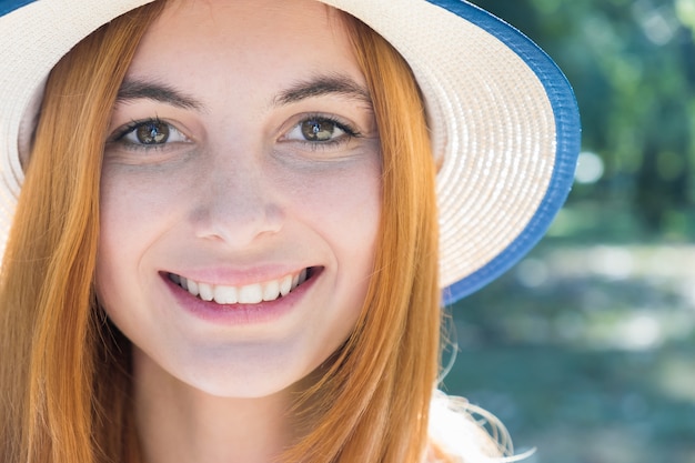 Portrait of gorgeous smiling teenage girl in yellow hat and with red hair outdoors on sunny summer day.