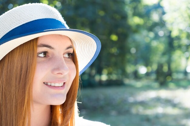 Portrait of gorgeous smiling teenage girl in yellow hat and with red hair outdoors on sunny summer day.