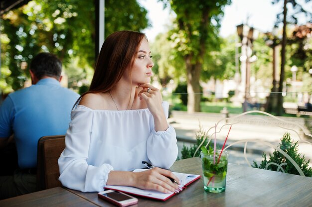 Ritratto di una bellissima giovane imprenditrice di successo scrivendo qualcosa nel suo quaderno rosso mentre era seduto in un caffè.