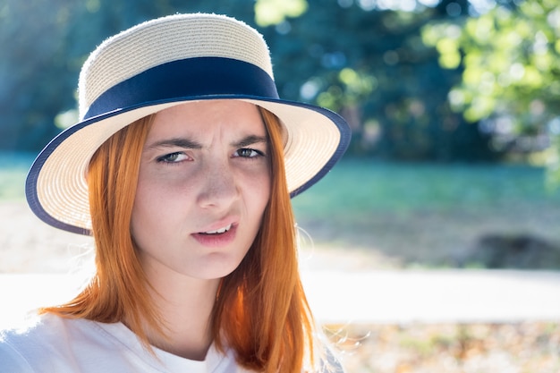 Portrait of gorgeous teenage girl in yellow hat and with red hair outdoors on sunny summer day.