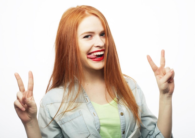 Portrait of gorgeous woman looking at camera with smile and\
showing peace sign with fingers