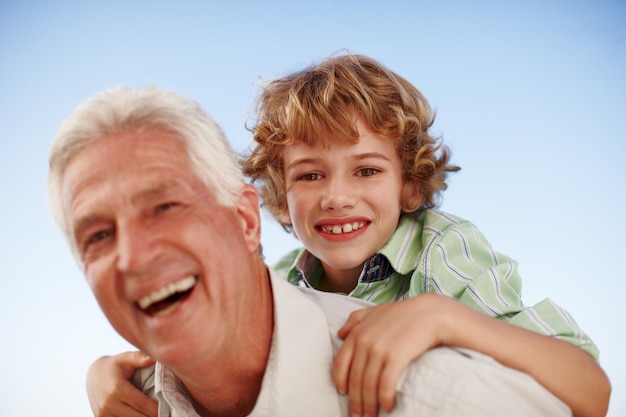 Portrait grandfather and boy with a smile piggy back and bonding outdoor sky and happiness Face happy grandad and male grandchild with joy loving and care with relationship cheerful and family