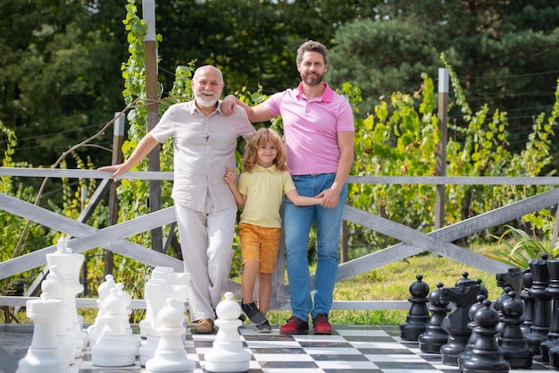 Portrait of grandfather father and son playing chess Happy men in different ages playing chess board game Three men generation