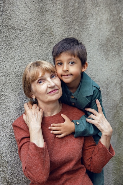 Portrait of a grandmother and grandson against a gray wall on street