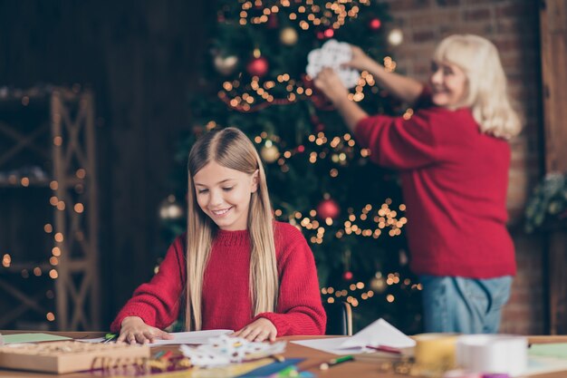 Portrait of granny grandchild hanging paper flake creating festive decor on table decorated house