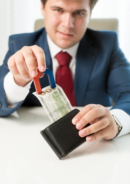 Portrait of greedy businessman pulling money out wallet with use of magnet