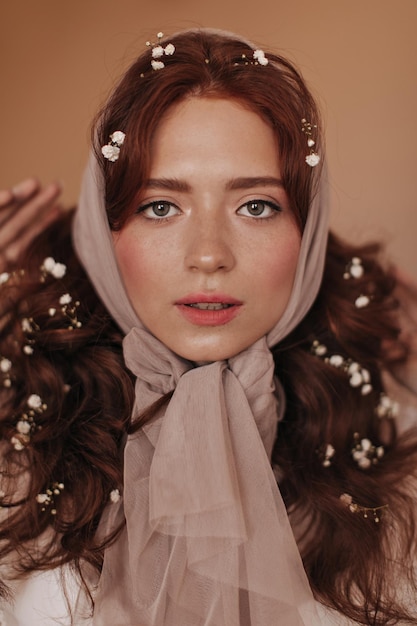 Portrait of greeneyed girl with small white flowers in her hair Woman in scarf looks into camera