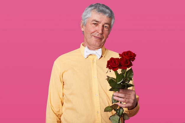 Portrait of grey haired elderly man in yellow shirt and white bow tie