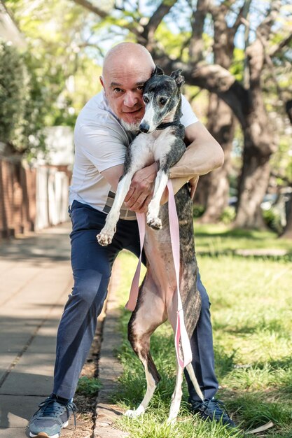 Foto ritratto di un cane levriero con il suo proprietario che lo abbraccia alla luce del sole