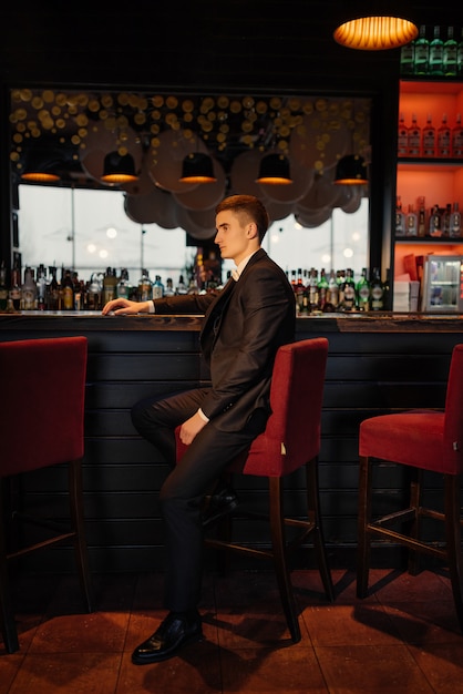 Portrait of a groom sitting on a chair by the bar. Low key.