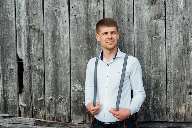 Portrait of a groom in a white shirt standing near the a wooden wall. Rustic style