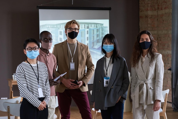 Portrait of group of business people in masks looking at camera\
while visiting business conference