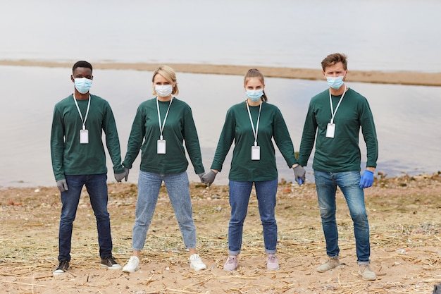 Foto ritratto di un gruppo di volontari in maschere protettive mano nella mano mentre si trovava sulla riva del fiume all'aperto