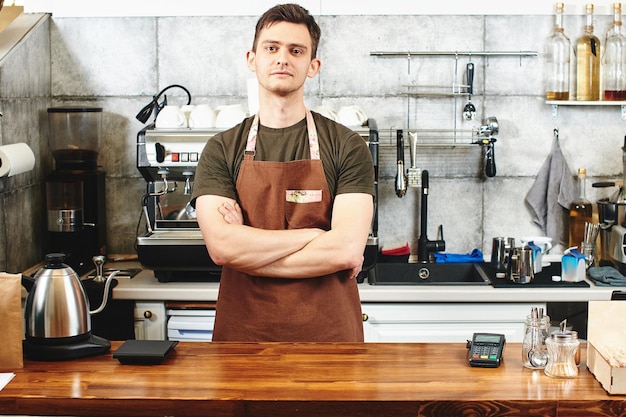 The portrait of the guy baristas at workplace on background of coffee