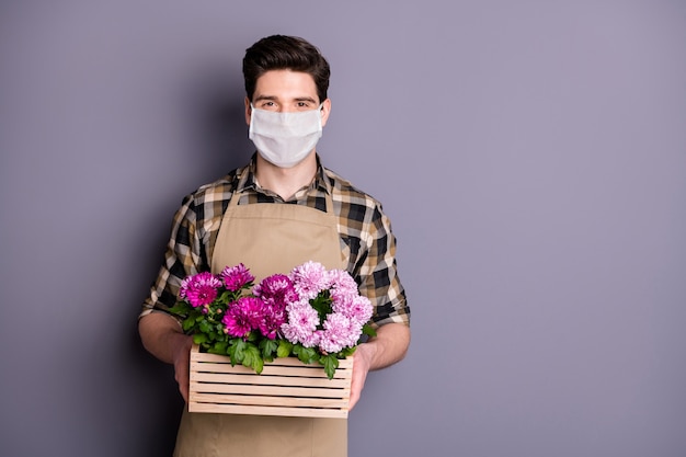남자 정원사의 초상화는 안전 마스크를 착용하고 꽃 냄비를 멈추고 예방 조치를 취합니다.