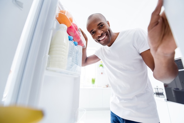 portrait of guy looking in fridge taking snack health care lifestyle regime in kitchen indoors