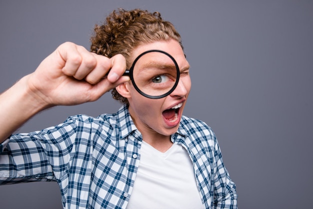 Portrait of guy wavy hair in checkered shirt showing big eye through loupe