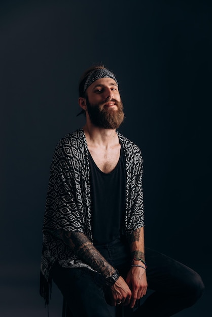 Photo portrait of a guy with a beard and tattoos on a dark background hipster