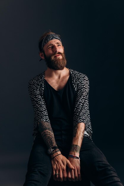 Photo portrait of a guy with a beard and tattoos on a dark background hipster