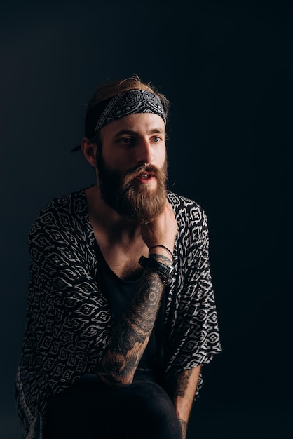 Foto ritratto di un ragazzo con la barba e tatuaggi su uno sfondo scuro hipster