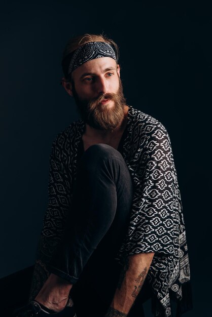 Photo portrait of a guy with a beard and tattoos on a dark background hipster