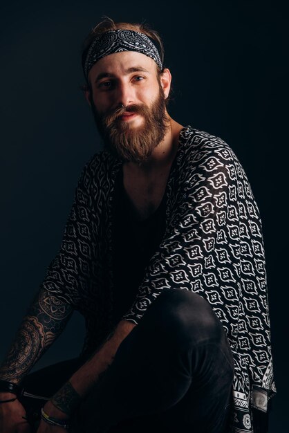 Foto ritratto di un ragazzo con la barba e tatuaggi su uno sfondo scuro hipster