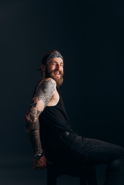 Photo portrait of a guy with a beard and tattoos on a dark background hipster