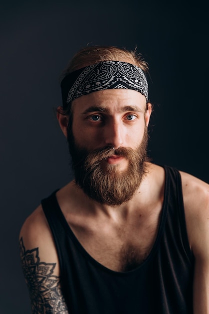 Foto ritratto di un ragazzo con la barba e tatuaggi su uno sfondo scuro hipster