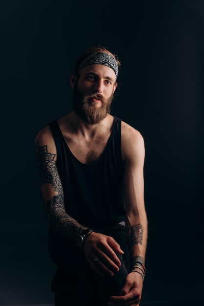 Photo portrait of a guy with a beard and tattoos on a dark background hipster