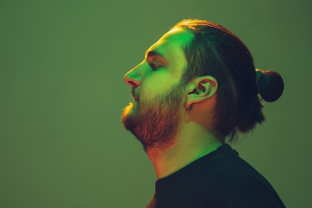 Portrait of a guy with colorful neon light on green studio background. Male model with calm and serious mood.