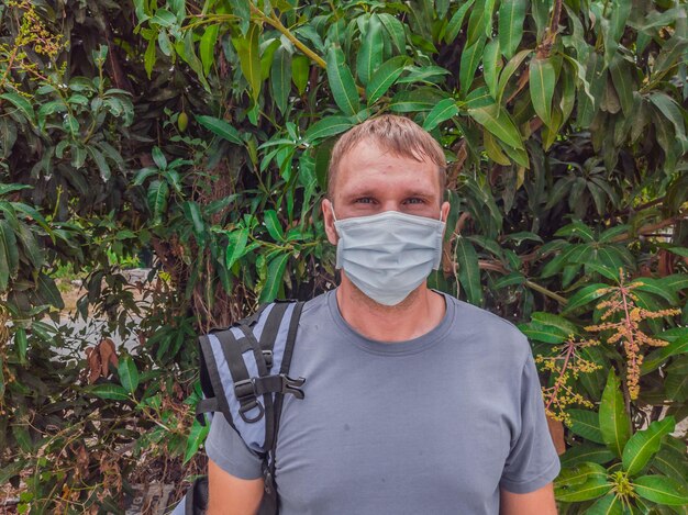 Portrait of guy with a medical mask Outside walking in the Mango trees garden He wants to breathe wait for the end of quarantine Covid19 isolation and beginning of normal life again