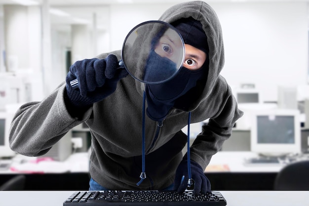 Portrait of hacker looking through magnifying glass in office