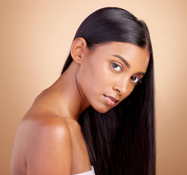 Portrait hair care and Indian woman with beauty cosmetics and dermatology on a brown studio background Face female person or model with volume skincare and scalp treatment with beauty and luxury