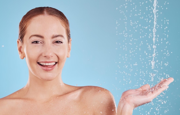 Portrait hand and water splash with girl for skincare in studio or blue background with face Woman shower and sustainability with drop for beauty routine with cosmetics or dermatology with smile