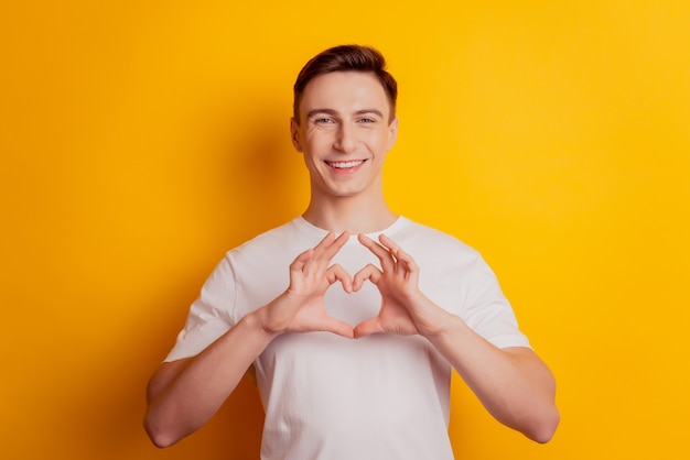 Portrait of handsome affectionate guy hands show heart love symbol on yellow background