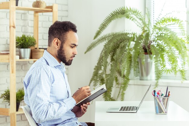 Portrait of handsome African black young business man working on laptop at office