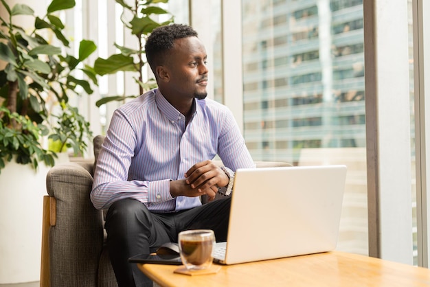 Portrait of handsome African businessman sitting in coffee shop using laptop computer