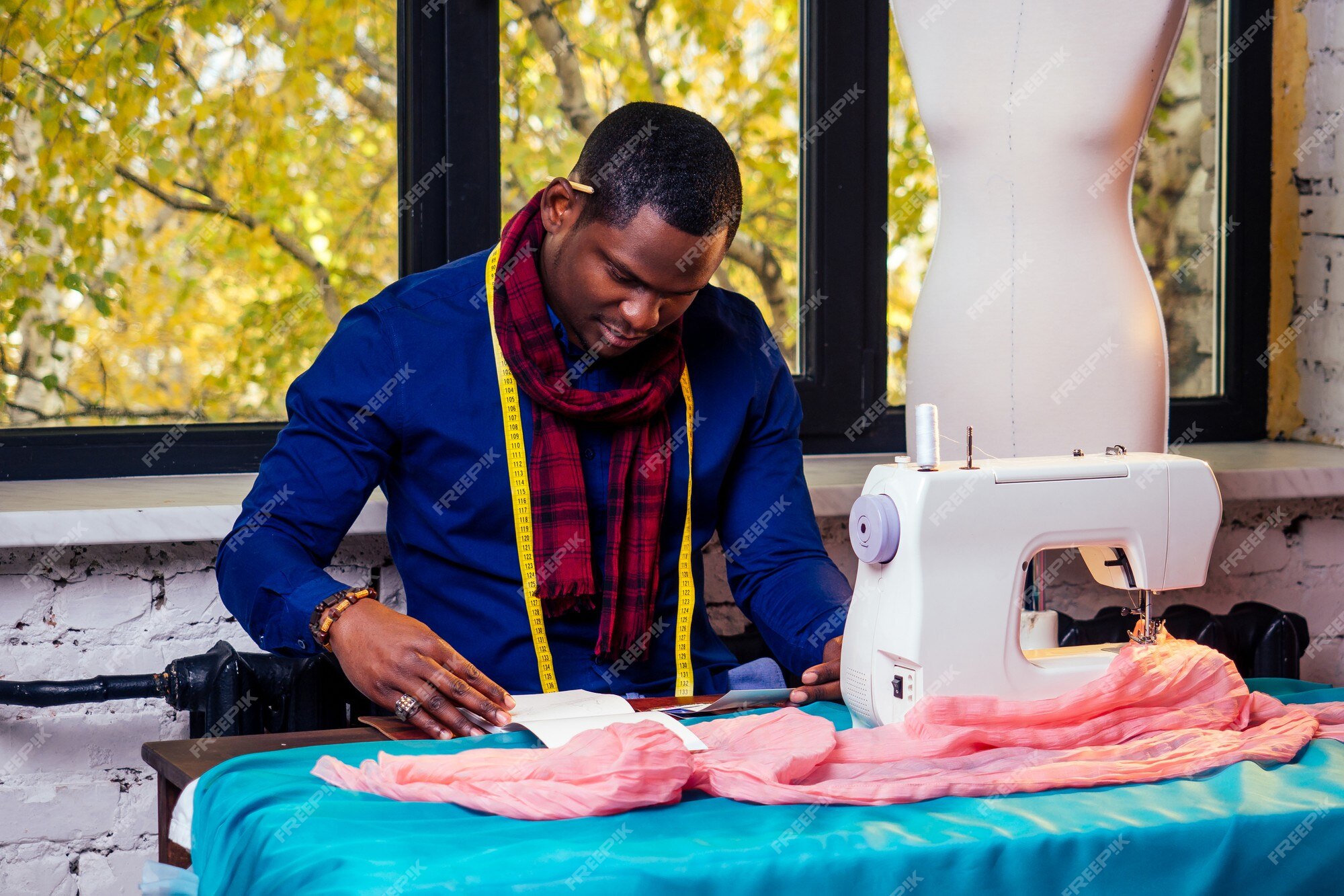 Premium Photo | Portrait of a handsome african man smiling seamstress with sewing   american man stylish designer working in tailor workshop  mannequin,table measuring tape in room against autumn window