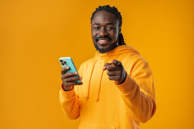 Photo portrait of handsome african man using his mobile agaist yellow background