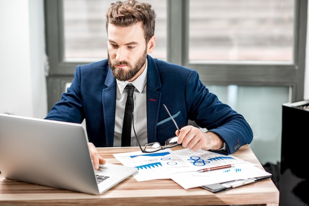 Portrait of a handsome analytic manager working with paper charts and laptop at the office