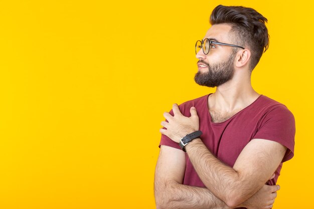 Portrait of a handsome arab young male student in burgundy shirt posing on a yellow wall