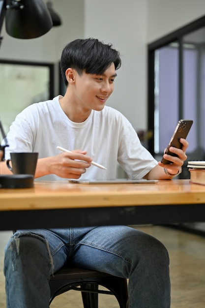 그의 스마트폰을 사용하여 그의 작업 책상에 세로 잘 생긴 아시아 남자