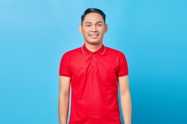 Portrait of handsome Asian man in red shirt and smiling happy looking straight ahead in good mood having auspicious day isolated on blue background