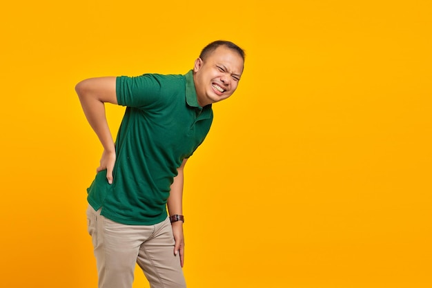 Portrait of handsome asian man suffering from back pain and touching back with hands