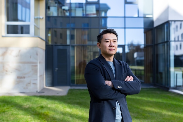Photo portrait handsome asian man a university college teacher businessman scientist or educator standing background modern office center or campus with arms crossed outside outdoors looking at camera
