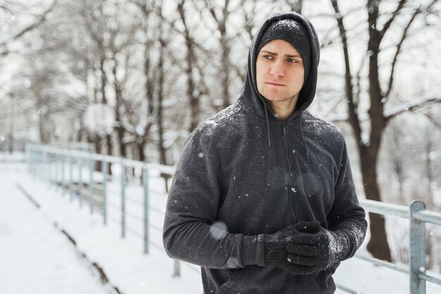 Portrait of handsome athletic man wearing hoodie during his winter workout in snowy city park