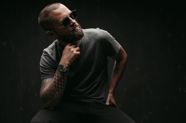 Portrait of a handsome balded man with long well trimmed beard wearing sunglasses and grey shirt looking away to side