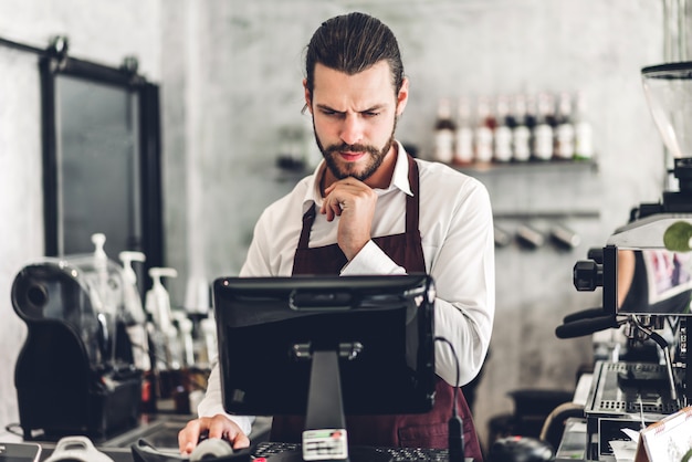 Portrait of handsome bearded barista man small business owner working behind the counter bar in a cafe