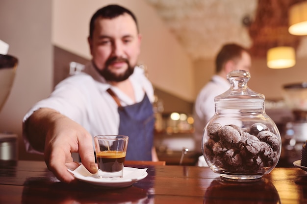 コーヒーショップとコーヒーマシンの背景にコーヒーを準備するハンサムなひげを生やしたバリスタの肖像画