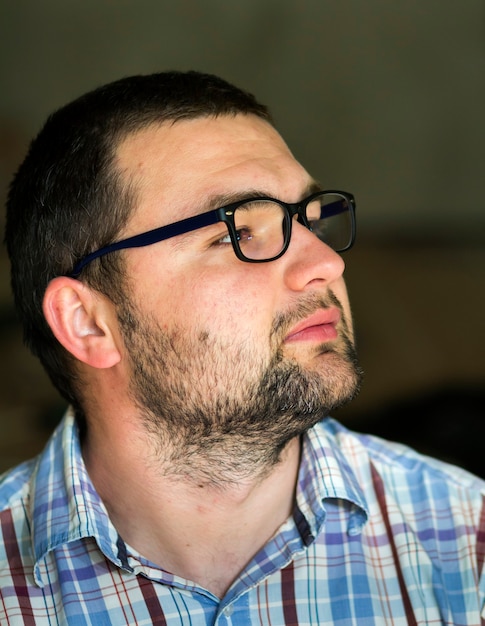 Portrait of handsome bearded black haired intelligent modern young man in glasses with short haircut and kind black eyes smiling in camera on blurred gray background. Youth and confidence concept.